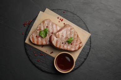 Photo of Delicious tuna steaks with sauce, parsley and spices on black table, top view