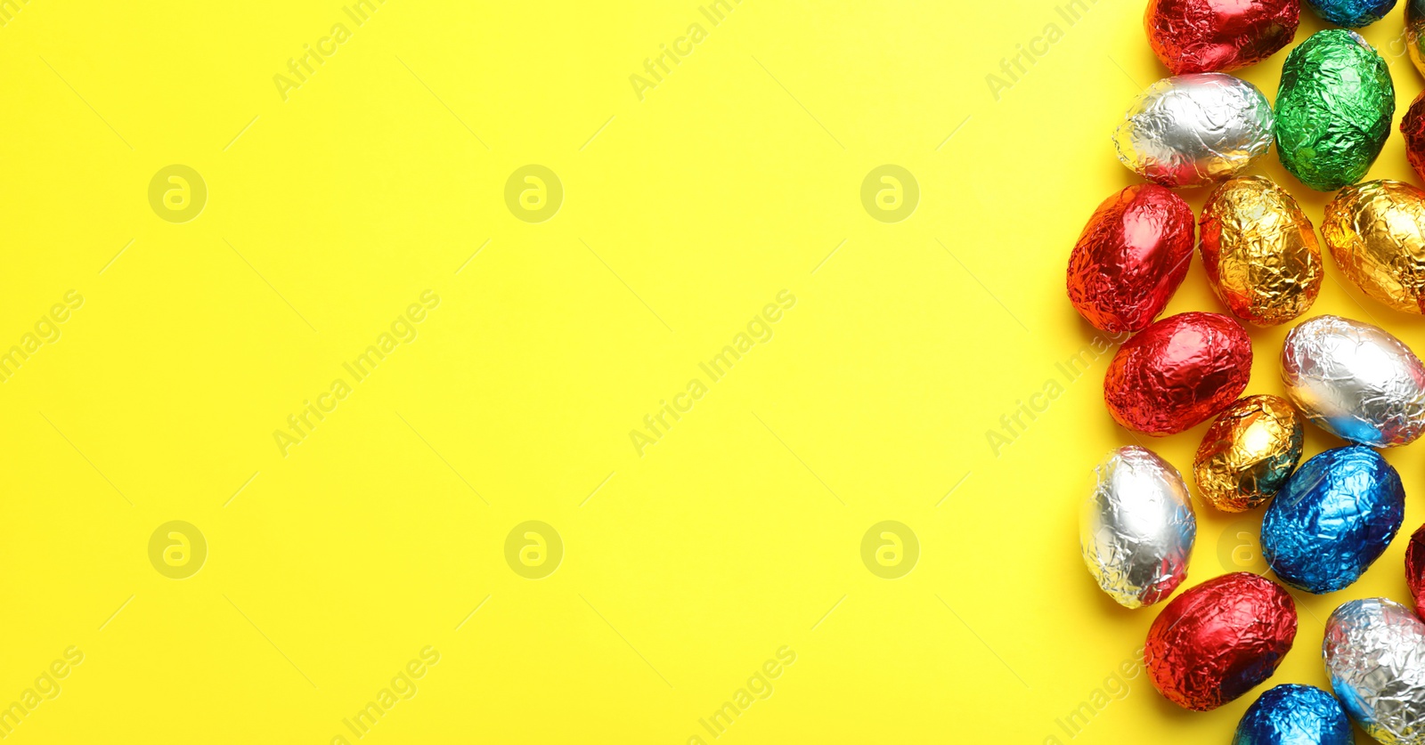 Photo of Chocolate eggs wrapped in colorful foil on yellow background, flat lay. Space for text