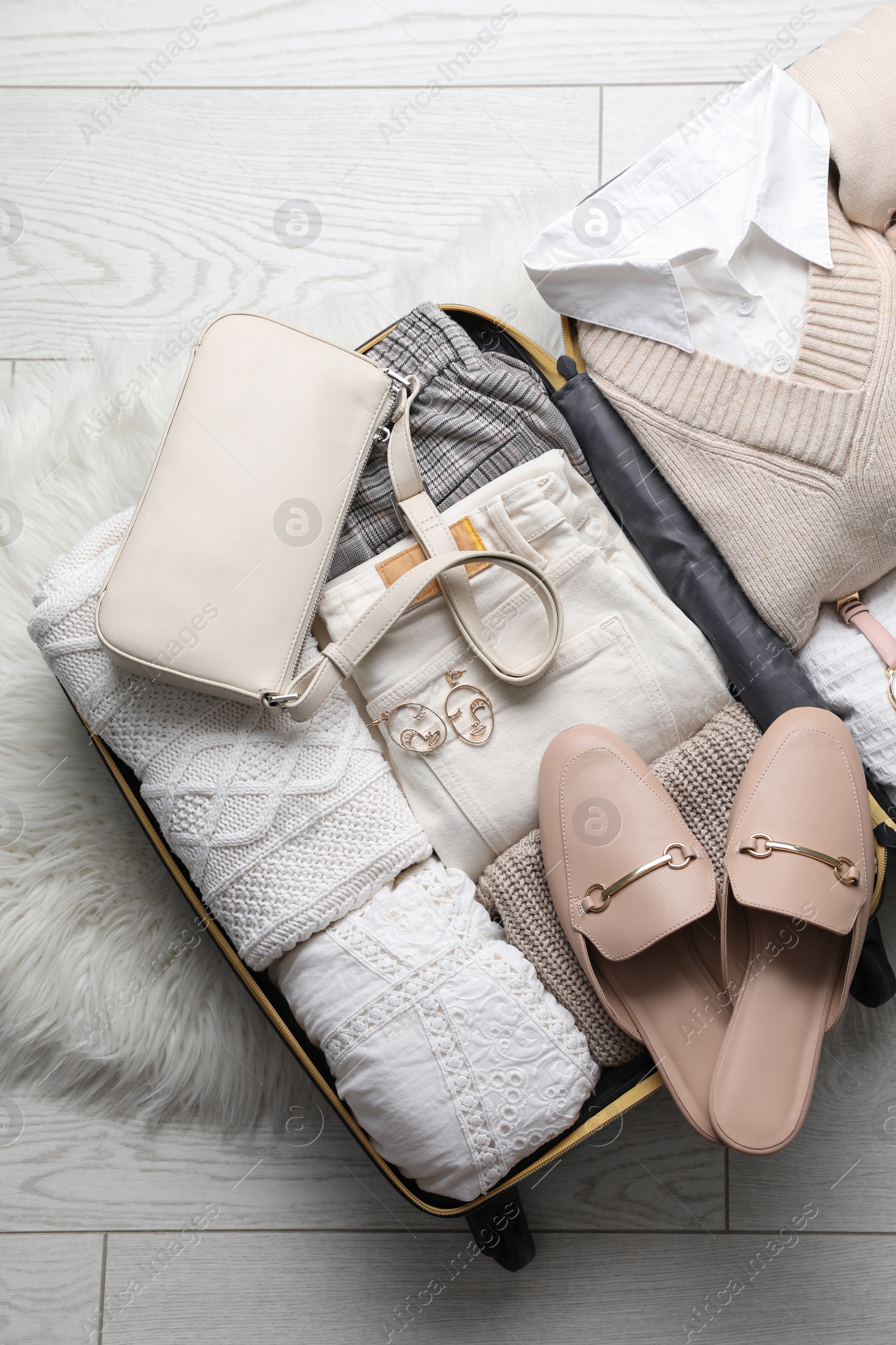 Photo of Open suitcase with folded clothes, shoes and accessories on floor, top view