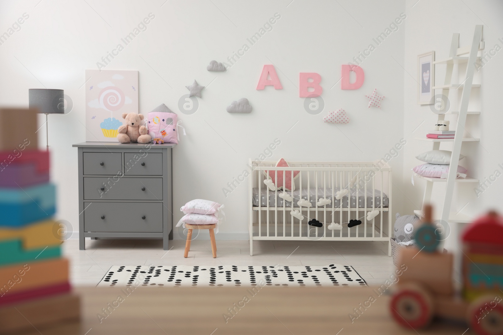 Photo of Cute baby room interior with crib and chest of drawers near white wall