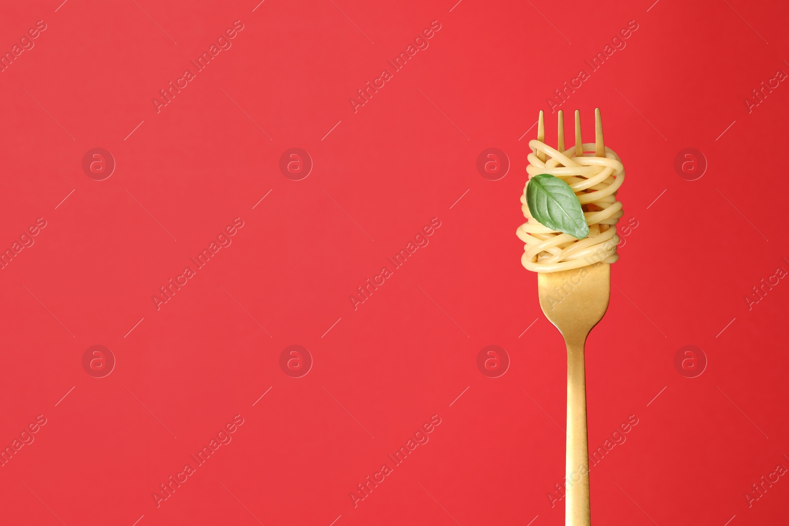 Photo of Fork with tasty pasta and basil on red background, space for text