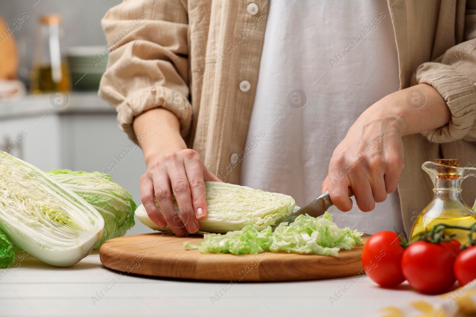 Photo of Woman cutting fresh chinese cabbage at white wooden table in kitchen, closeup