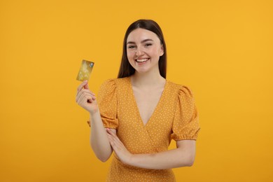 Happy woman with credit card on orange background