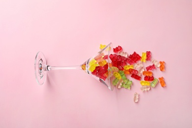 Photo of Martini glass with delicious color jelly bears on color background, top view