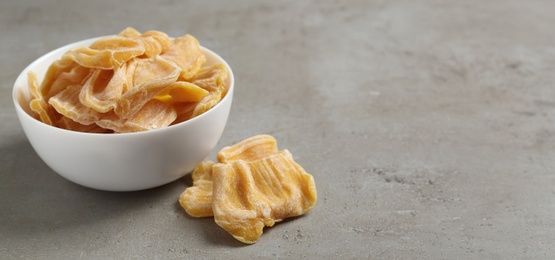 Photo of Delicious dried jackfruit slices on light grey table. Space for text
