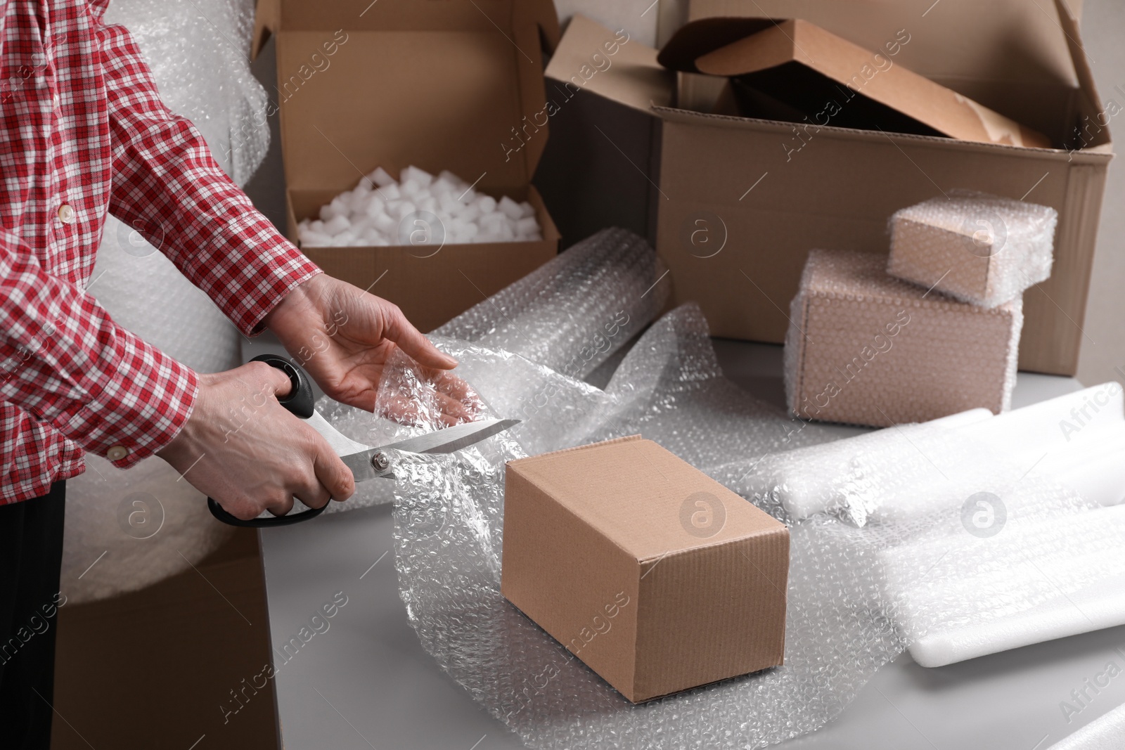 Photo of Woman cutting bubble wrap at table in warehouse, closeup