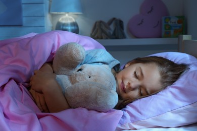 Photo of Cute little girl with toy bear sleeping in bed at home