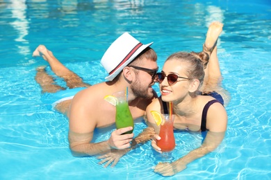 Photo of Young couple with refreshing cocktails in swimming pool at resort