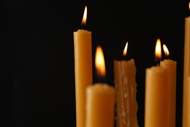 Many burning church candles on black background, space for text
