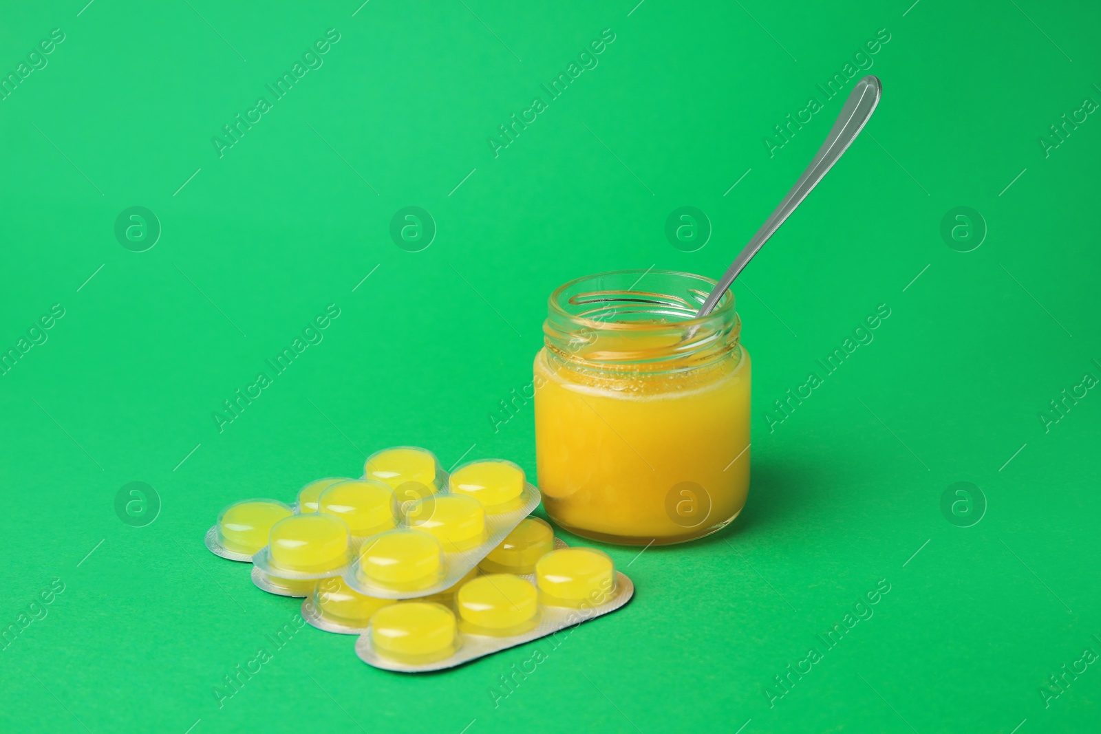 Photo of Blisters with cough drops and honey on green background