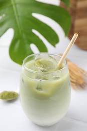 Photo of Glass of tasty iced matcha latte, leaf, bamboo whisk and powder on white tiled table