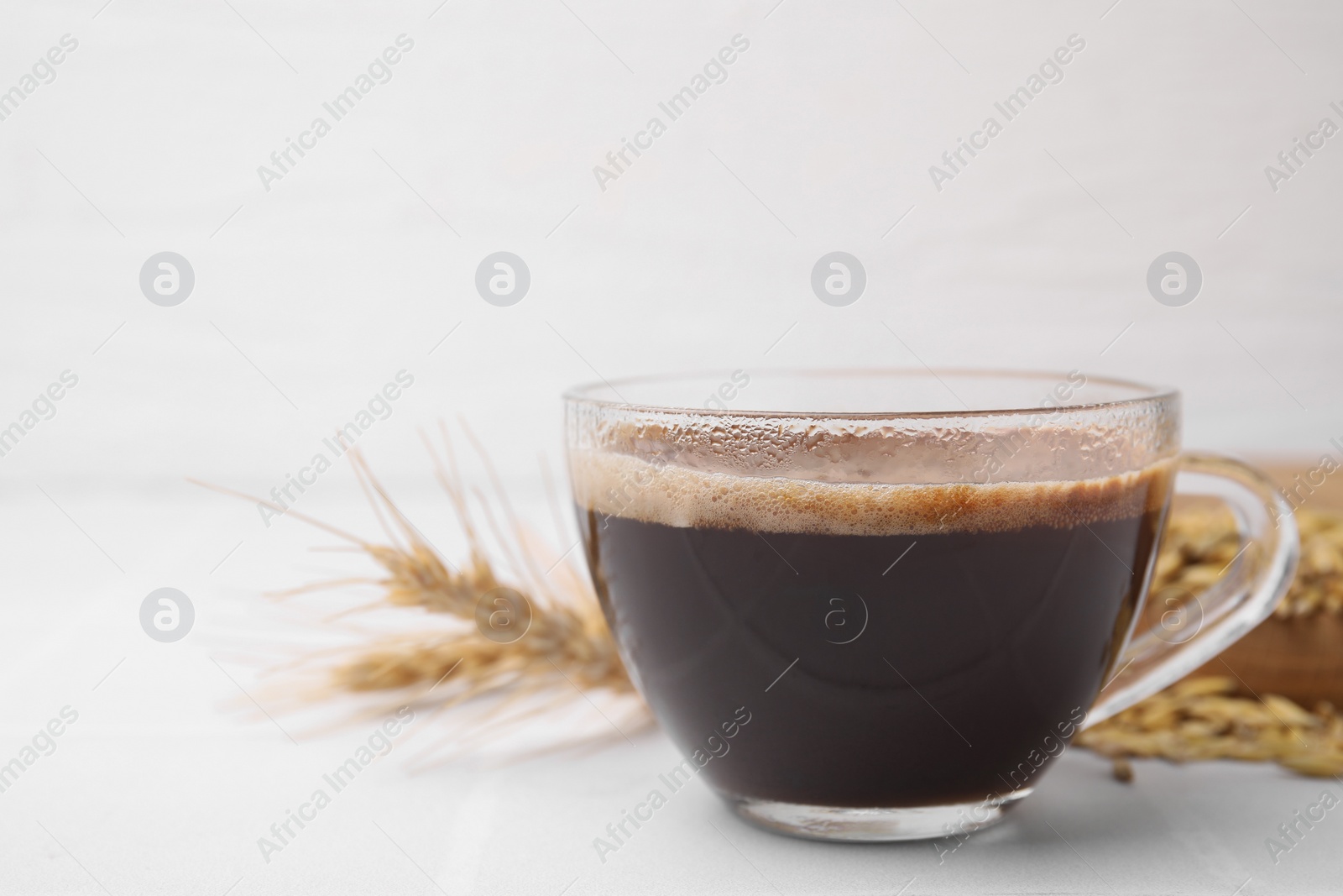 Photo of Cup of barley coffee and spike on white table, closeup. Space for text