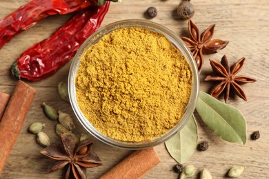 Photo of Curry powder in bowl and other spices on wooden table, flat lay