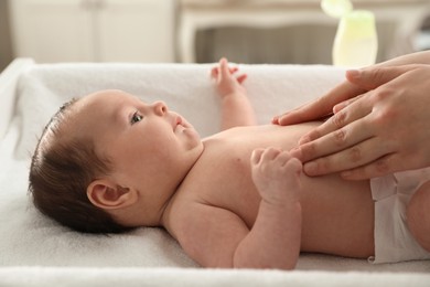 Mother massaging her cute baby with oil indoors, closeup