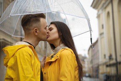 Photo of Lovely young couple with umbrella kissing on city street
