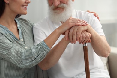 Photo of Senior man with walking cane and young woman indoors, closeup