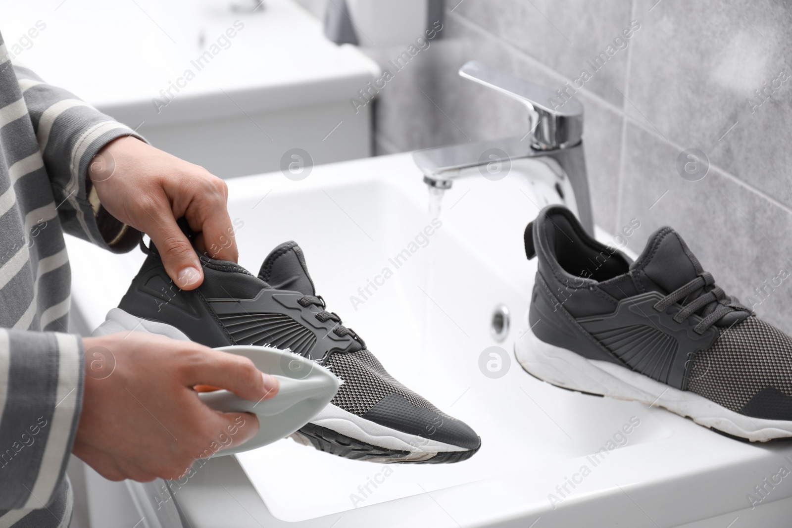 Photo of Woman washing stylish sneakers with brush in sink, closeup