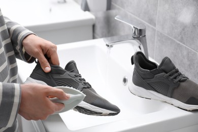 Woman washing stylish sneakers with brush in sink, closeup