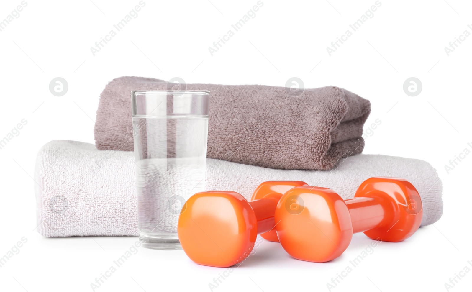 Photo of Stylish dumbbells, glass of water and towels on white background. Home fitness
