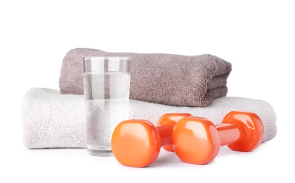 Stylish dumbbells, glass of water and towels on white background. Home fitness