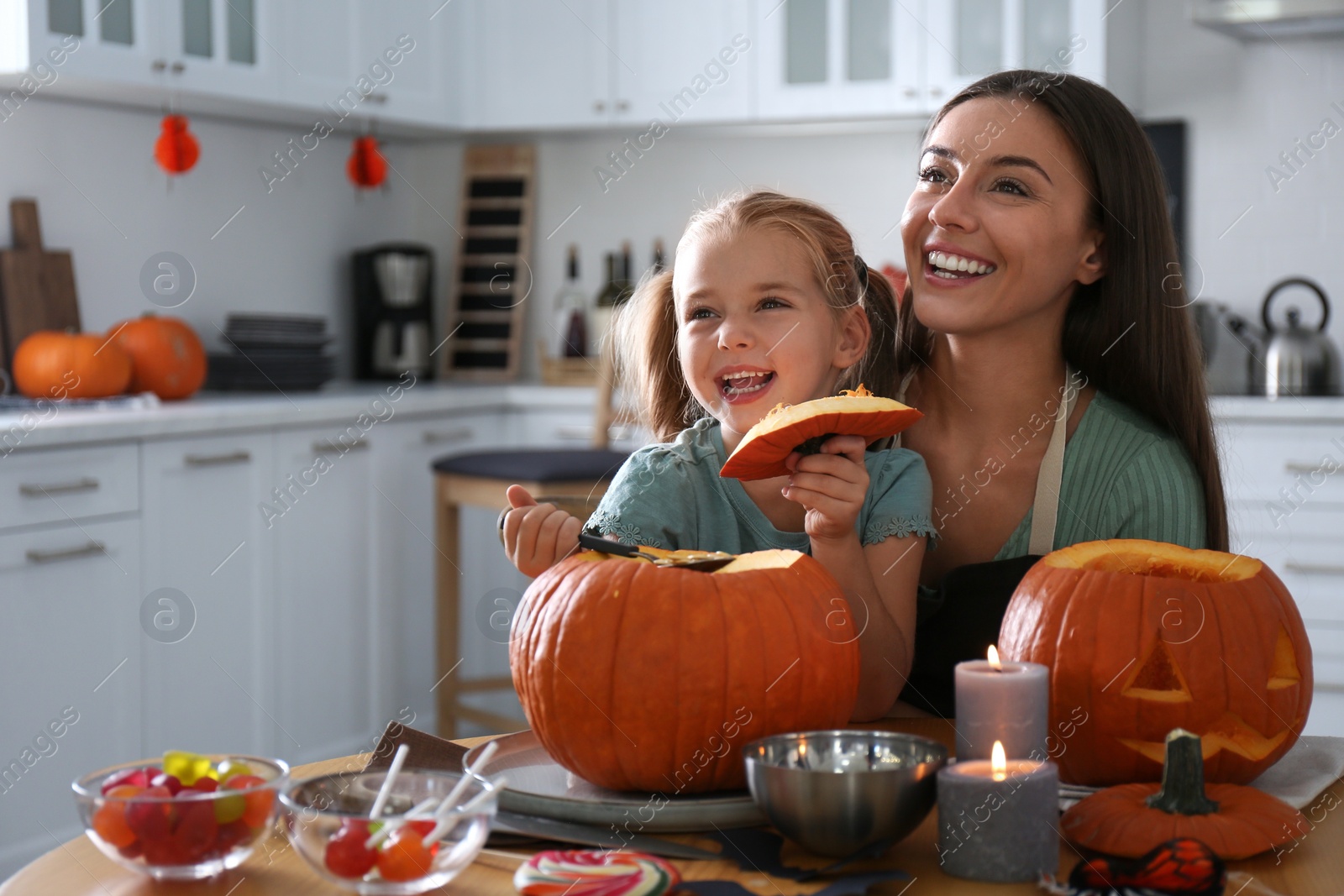 Photo of Mother and daughter making pumpkin jack o'lantern at table in kitchen. Halloween celebration