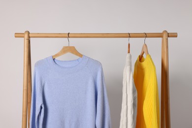 Rack with different warm sweaters on light background