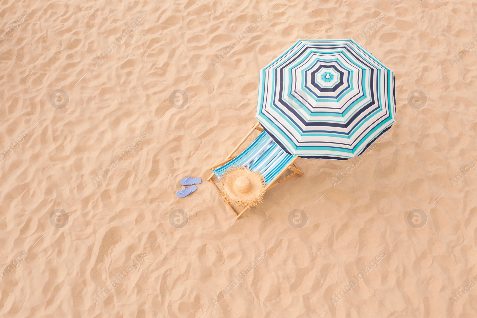 Image of Striped beach umbrella near sunbed with vacationist's stuff on sandy coast, aerial view