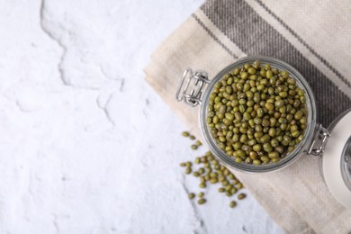 Photo of Glass jar with green mung beans on white textured table, flat lay. Space for text