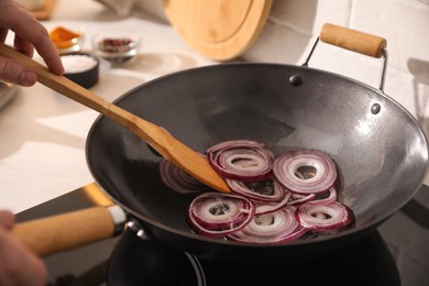 Man stirring onion slices in frying pan, closeup