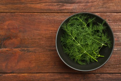 Photo of Bowl of fresh green dill on wooden table, top view. Space for text