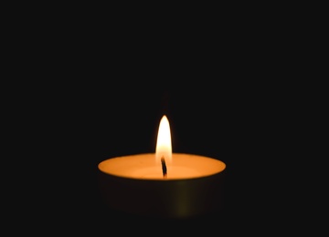 Photo of Bright burning candle in darkness. Funeral symbol