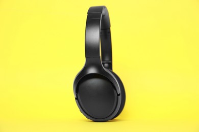 Photo of Modern black wireless headphones on yellow background