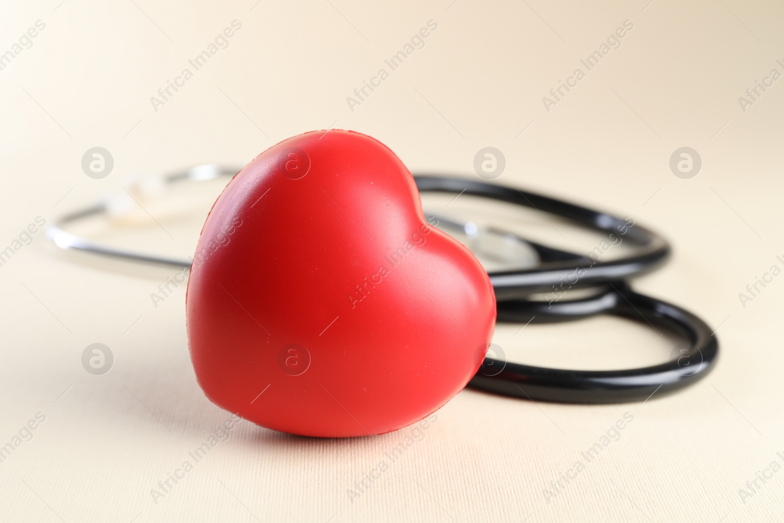 Photo of Stethoscope and red heart on beige background, closeup