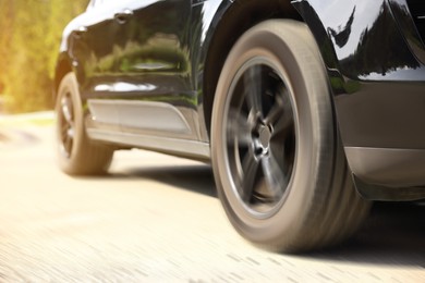 Black car driving on road outdoors, closeup with motion blur effect. Space for text