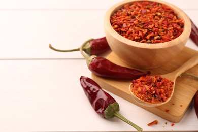 Photo of Chili pepper flakes and pods on white wooden table, closeup. Space for text