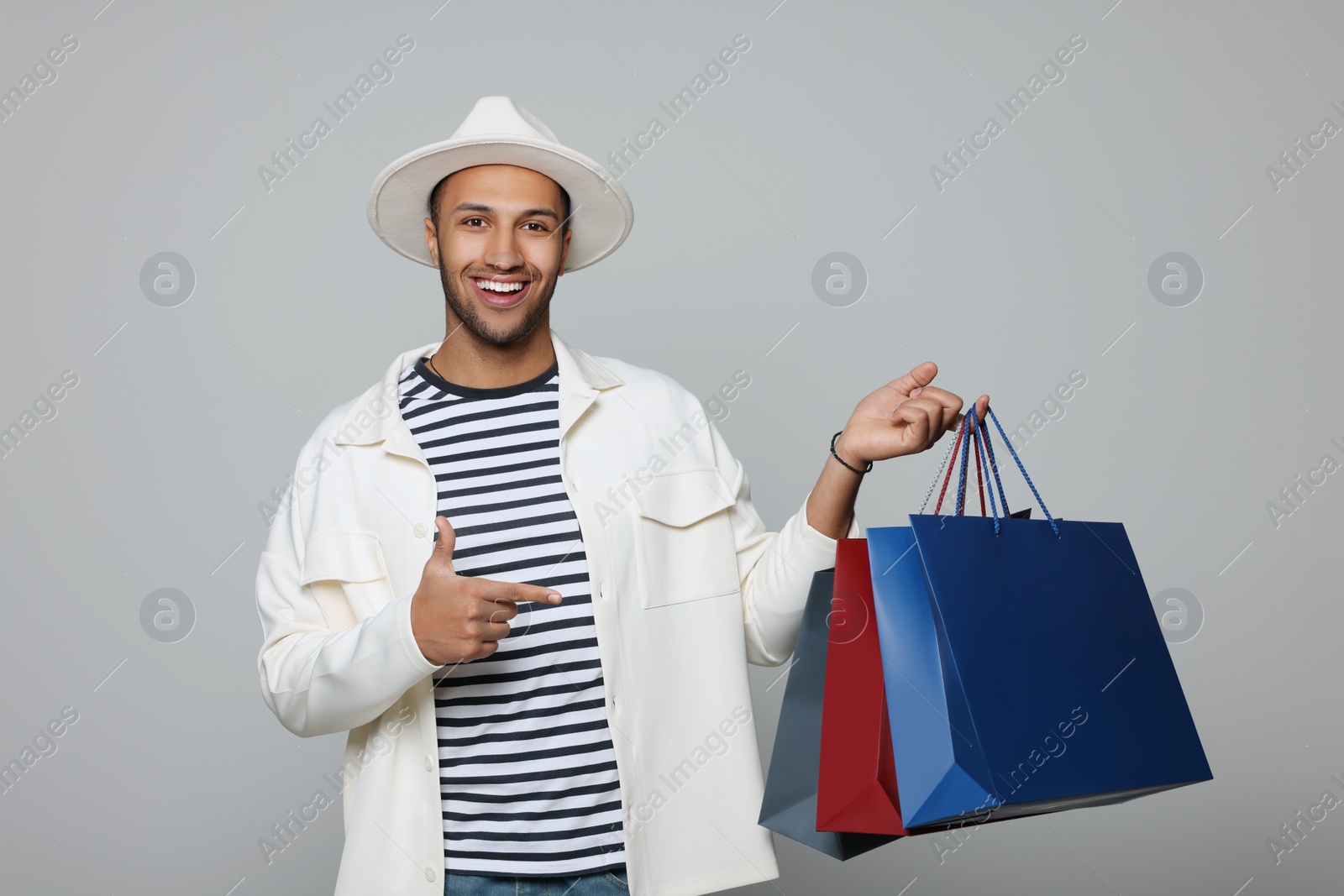 Photo of Happy African American man in hat with shopping bags on light grey background