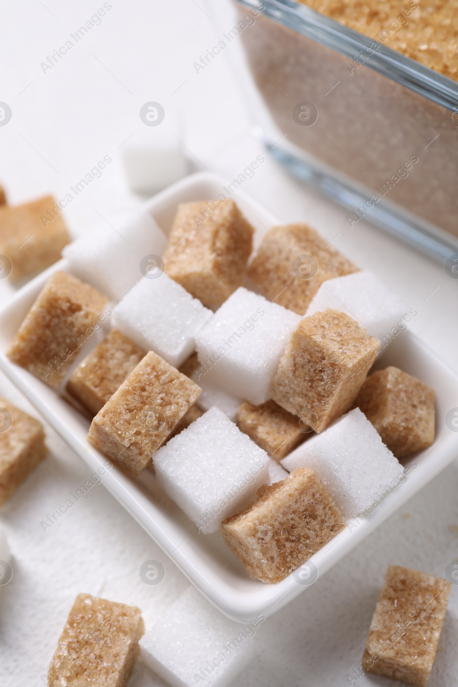 Photo of Different sugar cubes in bowl on white table, closeup