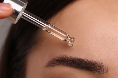 Young woman applying essential oil onto face, closeup