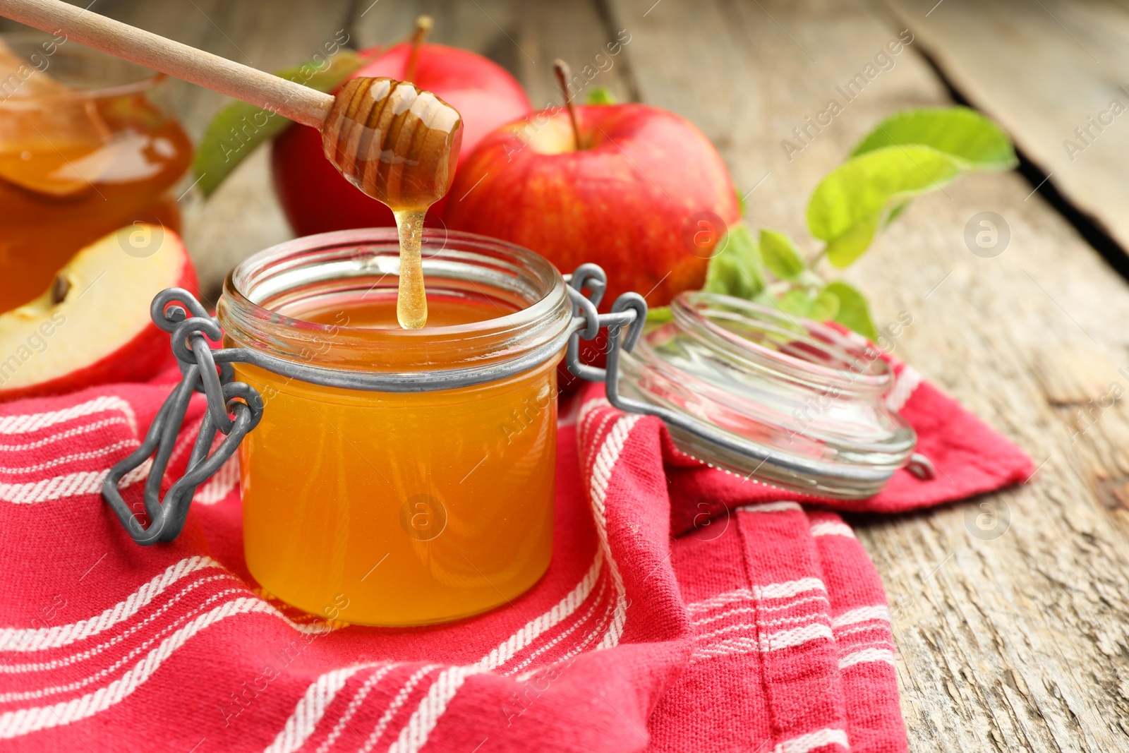 Photo of Dripping sweet honey from dipper into jar and fresh apples on wooden table, selective focus. Space for text