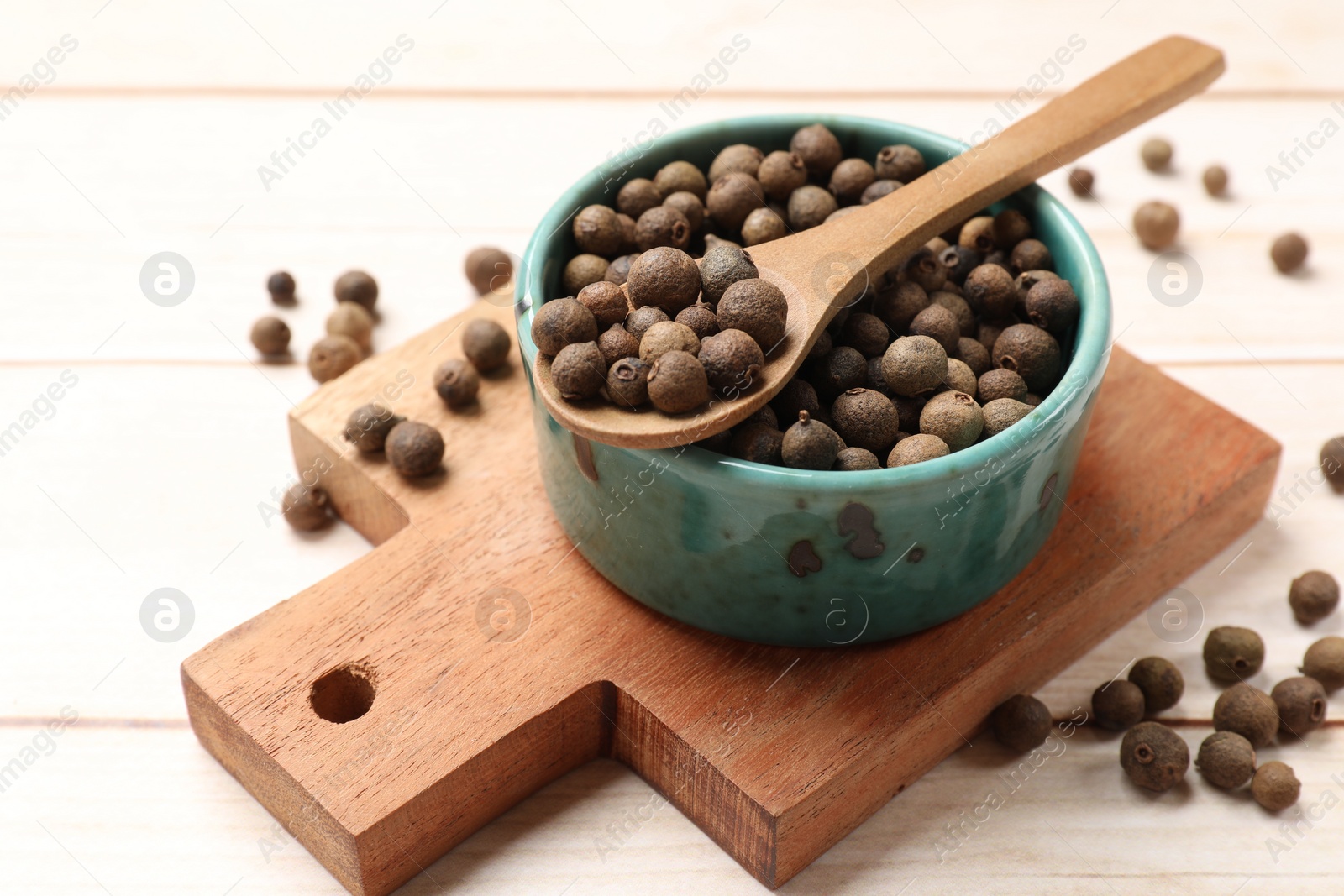 Photo of Dry allspice berries (Jamaica pepper) in bowl and spoon on light wooden table, closeup
