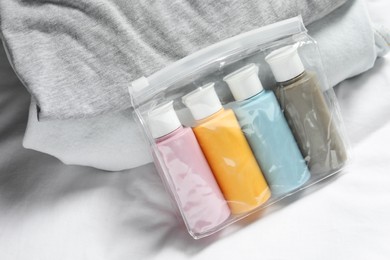 Cosmetic travel kit. Plastic bag with small containers of personal care products and stack of clothes on bed