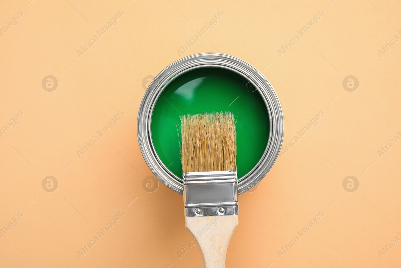 Photo of Open can with green paint and brush on light orange background, top view