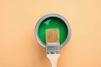 Photo of Open can with green paint and brush on light orange background, top view