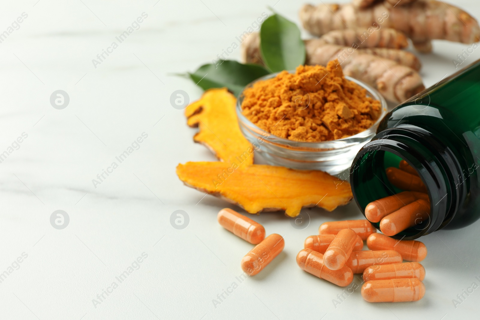 Photo of Aromatic turmeric powder, pills and raw roots on white marble table, closeup. Space for text