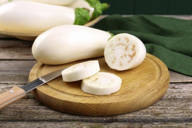 Board with raw eggplants and knife on wooden table