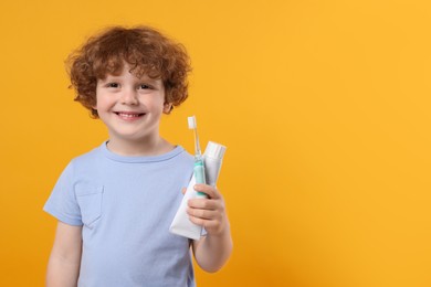 Photo of Cute little boy holding electric toothbrush and tube of toothpaste on yellow background, space for text