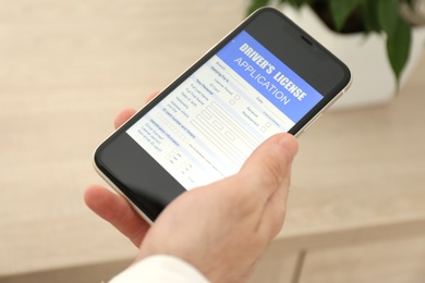 Man holding smartphone with driver's license application form at home, closeup