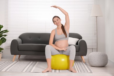 Photo of Pregnant woman doing exercises on fitness ball in room. Home yoga