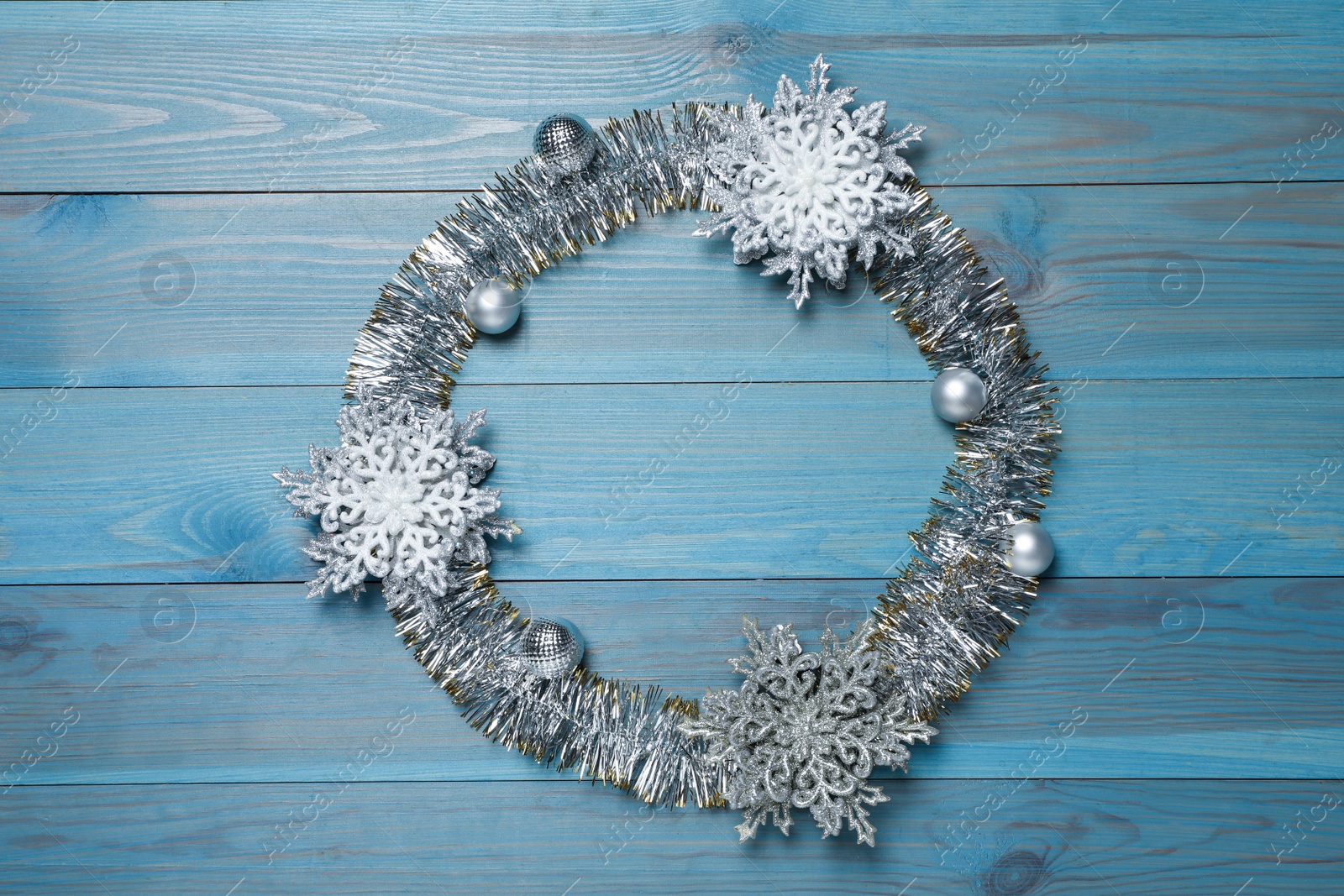 Photo of Frame of bright tinsel and Christmas decor on light blue wooden background, top view. Space for text