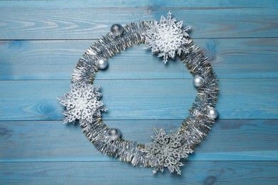 Frame of bright tinsel and Christmas decor on light blue wooden background, top view. Space for text